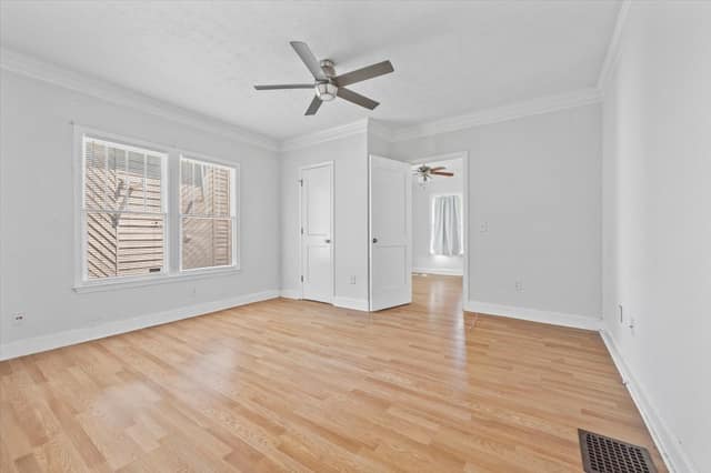 Primary bedroom with hardwood flooring, crown molding, ceiling fan, and paired windows