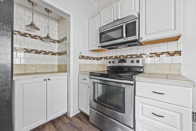 Kitchen with white cabinetry, stainless range and microwave, tile backsplash, and pendant lighting