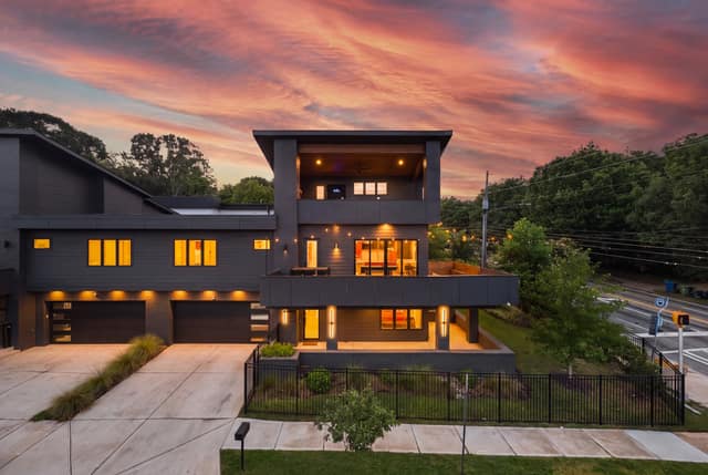Street-side elevation at twilight with illuminated terraces, two-car garage, and fenced grounds