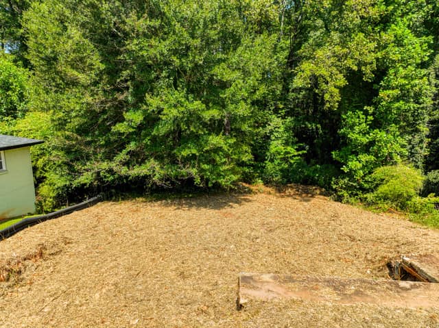View across the vacant lot toward mature trees with part of a neighboring home visible