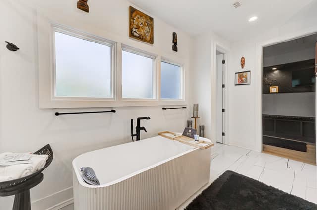 Fluted freestanding soaking tub beneath a bank of privacy windows