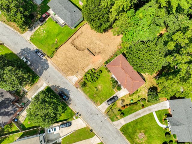 Aerial view of the vacant lot with surrounding homes and wooded areas