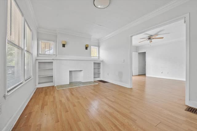 Living room with white brick fireplace, built-in shelving, and hardwood flooring opening to the adjoining room