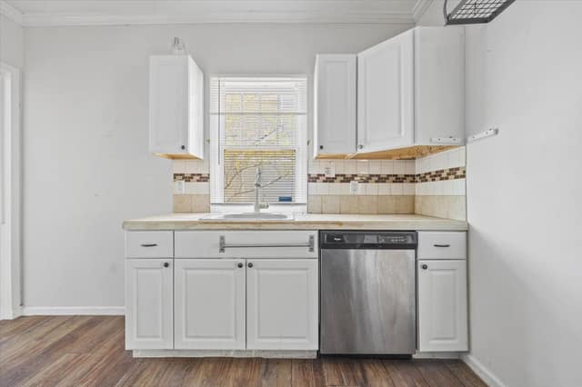 Kitchen sink wall with dishwasher, cabinetry, and window overlooking the yard